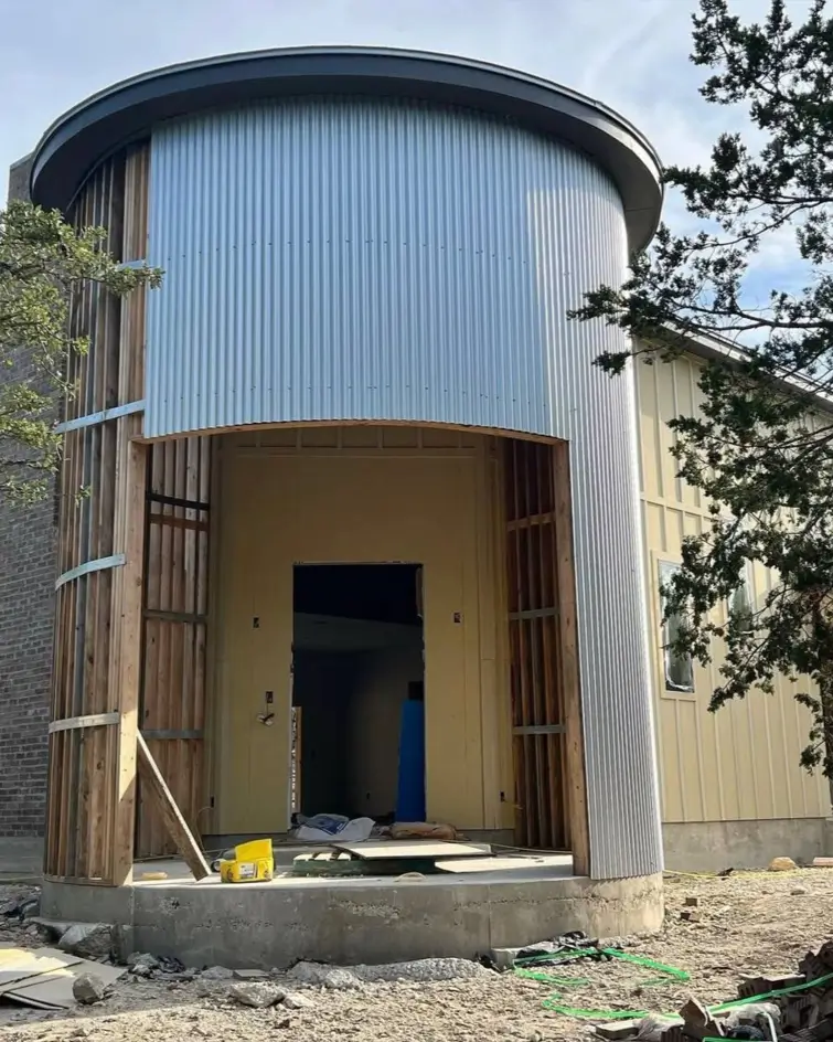 Corrugated metal siding being installed on the exterior of a custom-built silo house.