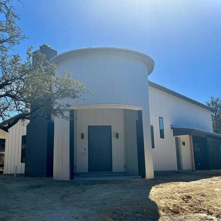 The nearly completed exterior of a white, custom-built silo house with a modern dark front door.