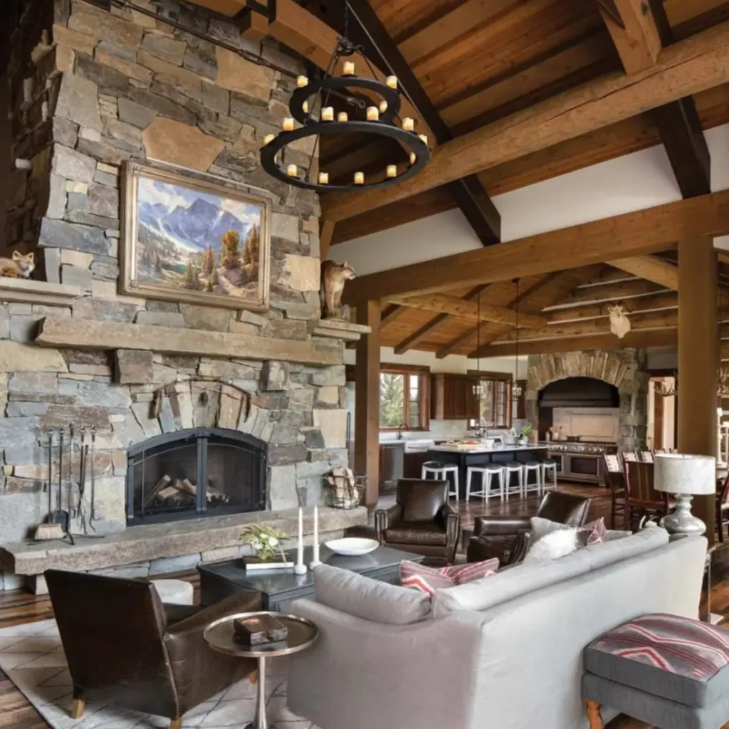 Grand log cabin living room with massive stone fireplace, high ceilings, and open kitchen.