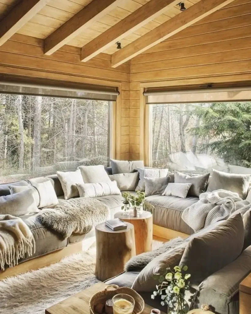 Cozy log cabin living room with large sectional sofa, many pillows, and forest views.