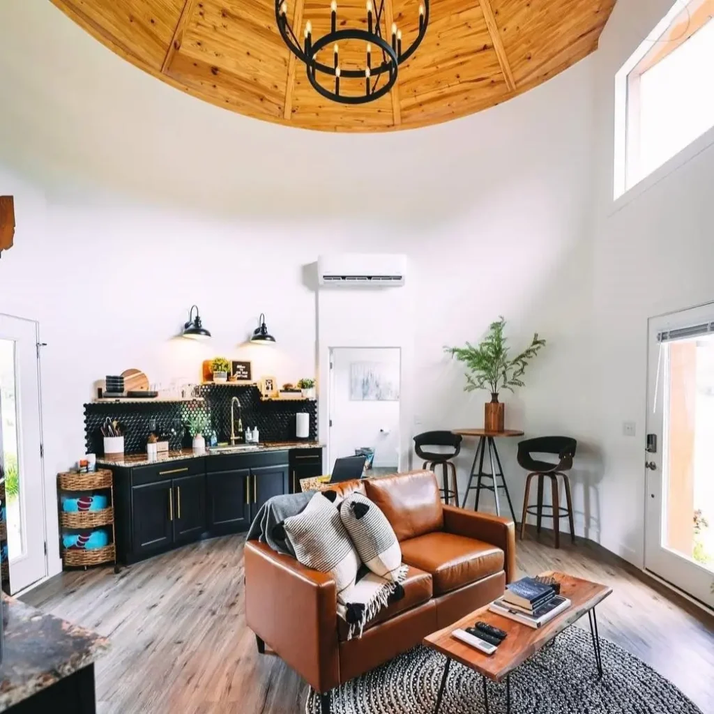 The open-plan living area of a silo home featuring a modern leather sofa on a round rug and a sleek black kitchenette.
