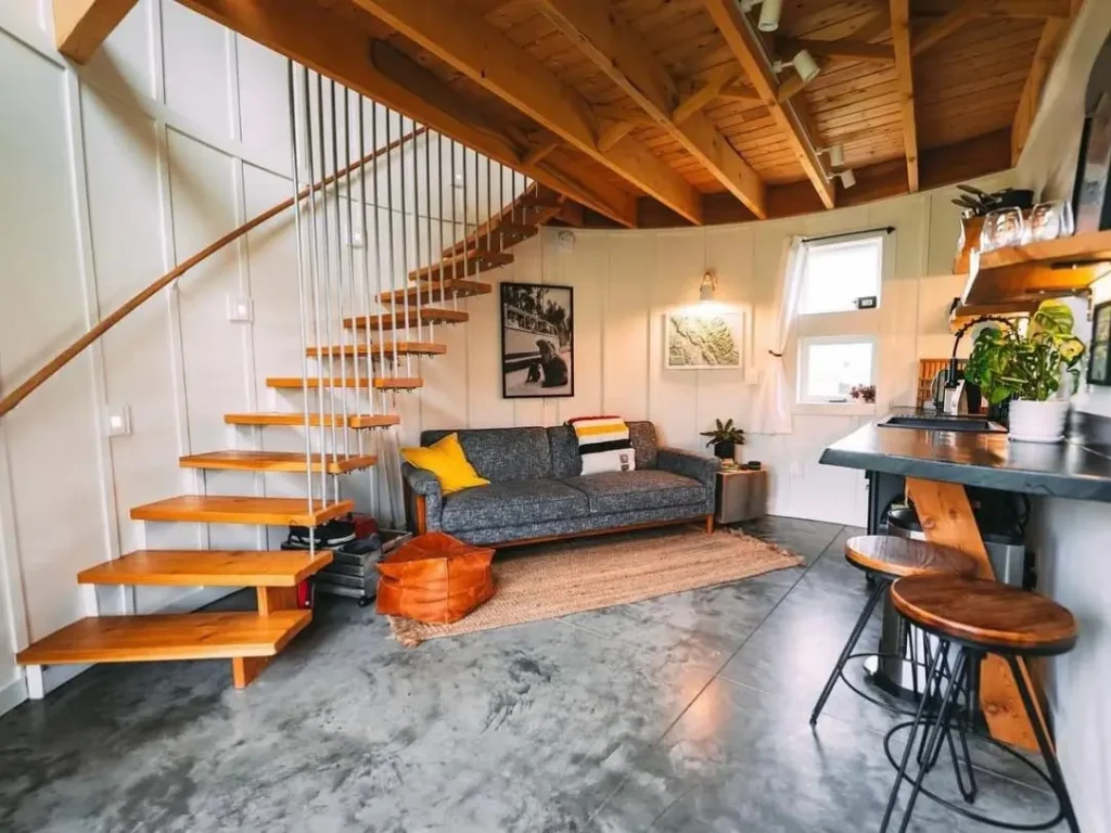 A modern, open-riser staircase with wood treads ascends along the curved wall of a silo home.