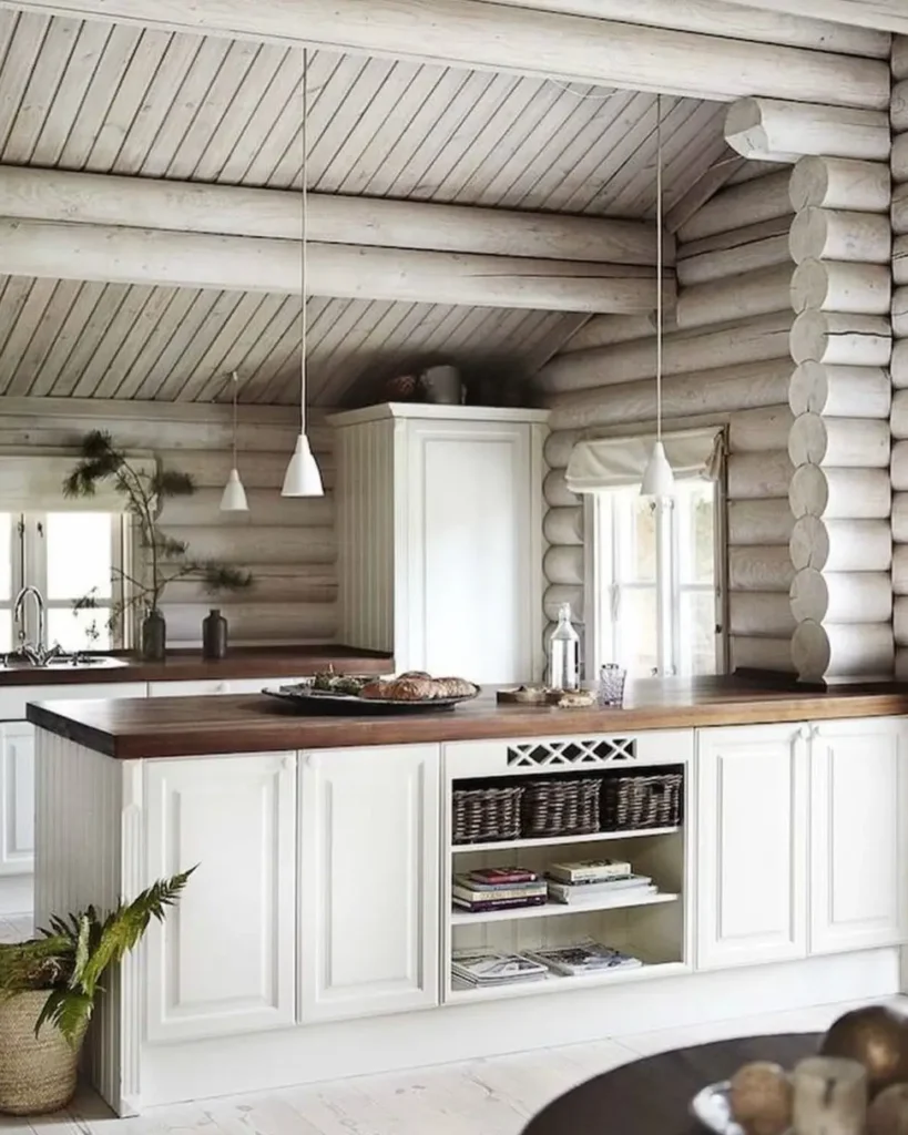 Modern log cabin kitchen with white-washed logs, white cabinets, and wooden countertops.