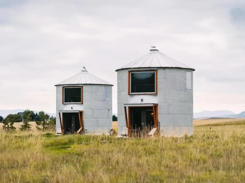 Two identical modern silo homes stand in a field, showcasing a clean, minimalist design ideal for guest accommodations.