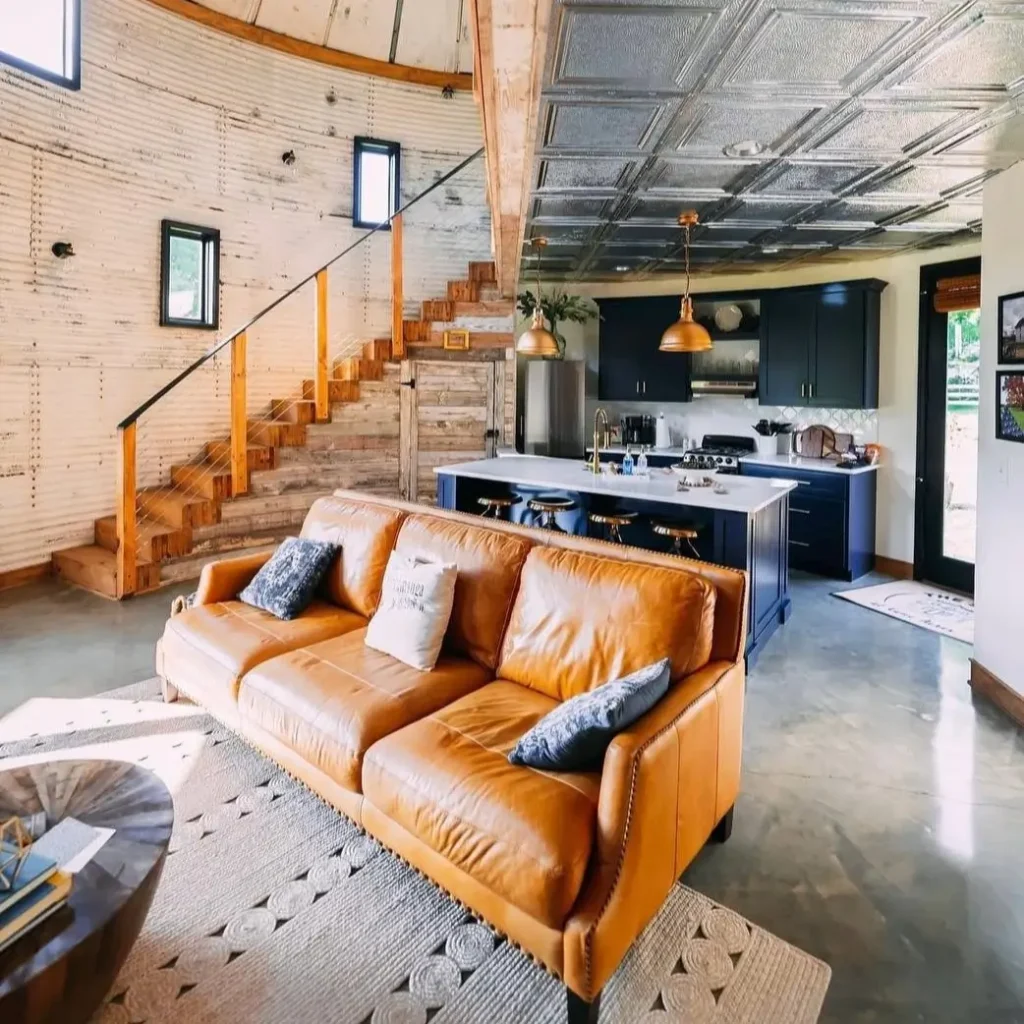 A spacious, open-plan silo home interior where the original, weathered metal walls are left exposed, complemented by a modern kitchen.