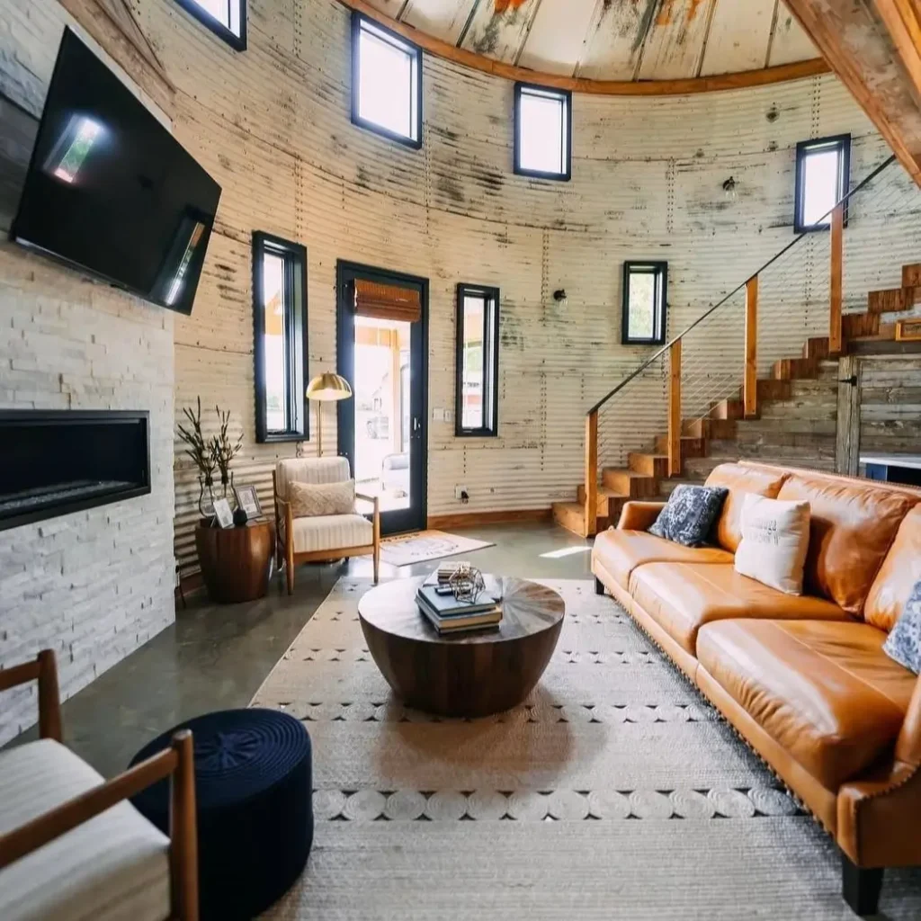 A wide view of a rustic-industrial silo living room, showcasing how a modern fireplace and comfortable seating can anchor a large, circular space.