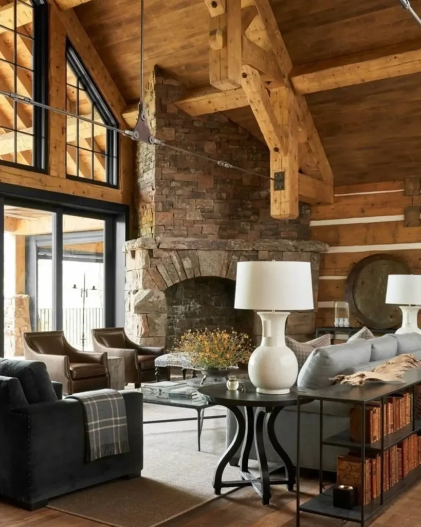 Modern log cabin living room with stone fireplace, exposed logs, and large windows.