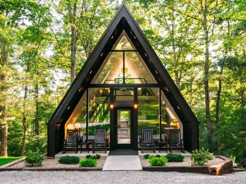 A symmetrical black A-frame cabin in Hocking Hills with a full glass front and a porch with rocking chairs.
