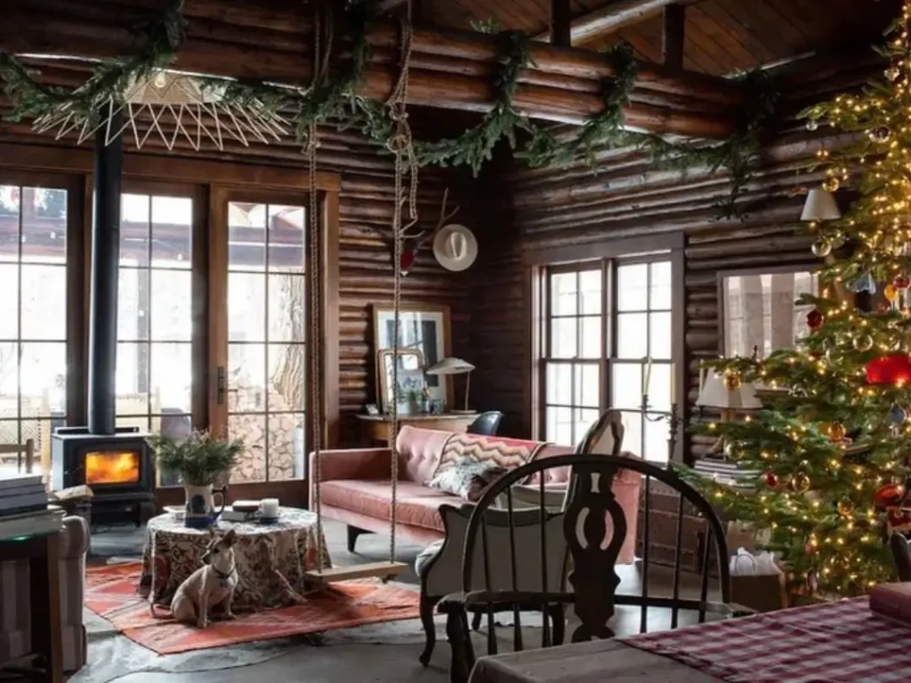 Cozy log cabin living room decorated for holidays with Christmas tree and wood stove.