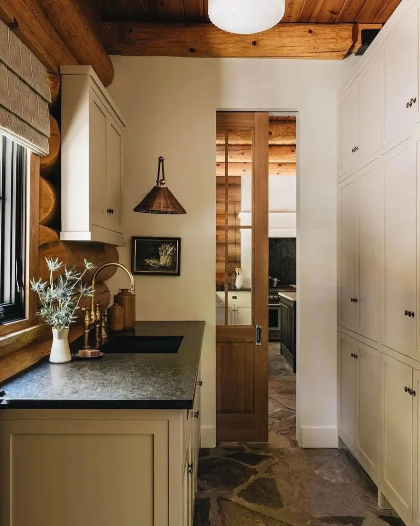 Log cabin kitchen with dark sink, white cabinets, and wooden sliding door.