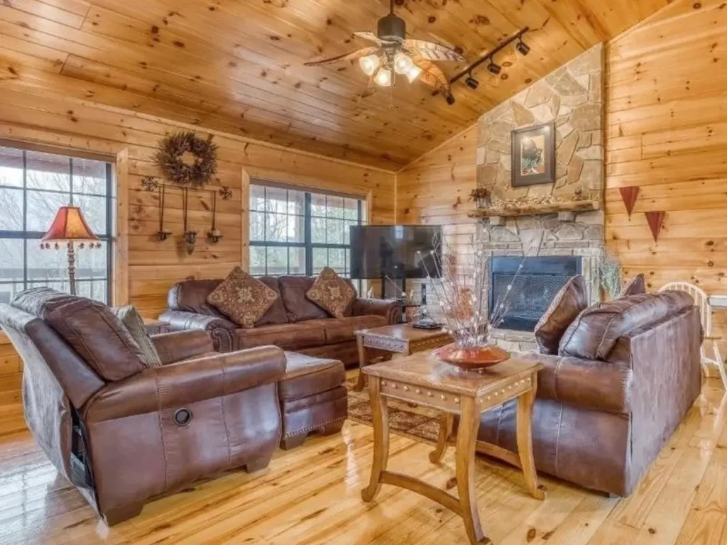 Cozy log cabin living room with stone fireplace, leather sofas, and wood walls.