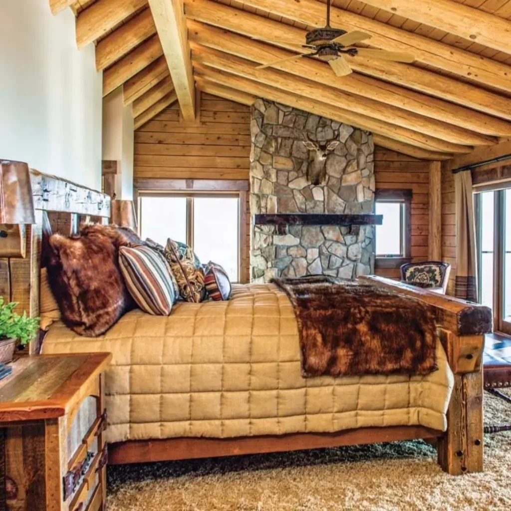 Cozy log cabin bedroom with wooden bed, stone fireplace, and rustic beams.