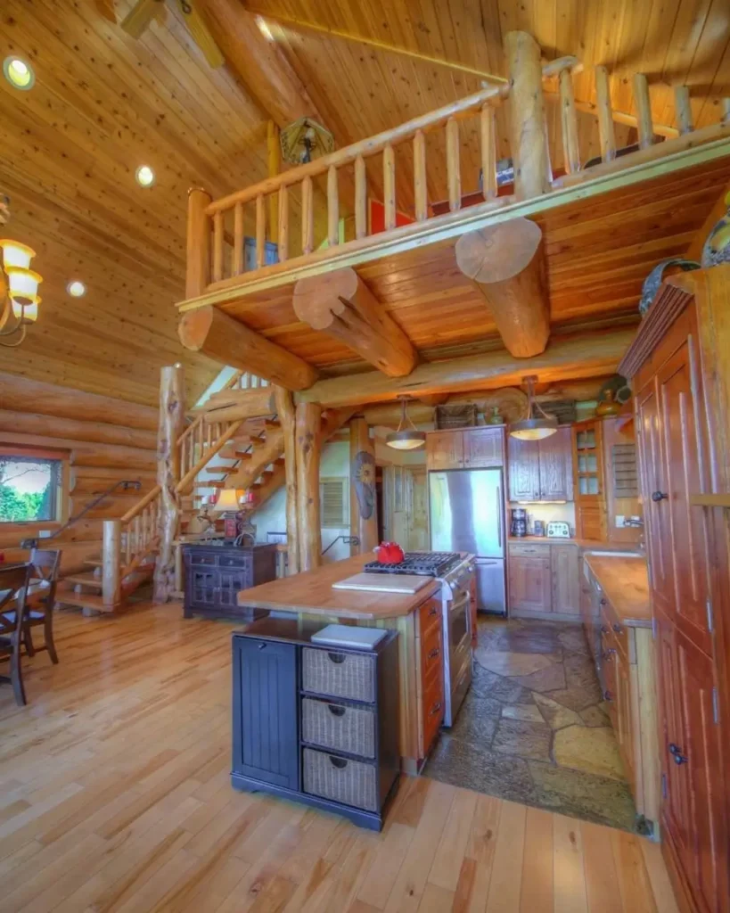 Log cabin interior with open loft, wooden staircase, and exposed log beams.