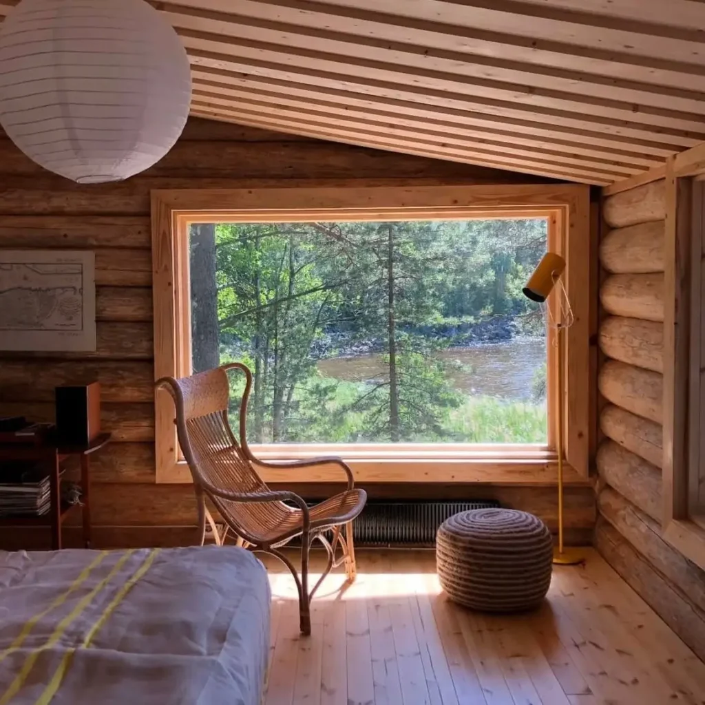 Cozy log cabin bedroom with large window overlooking a river.