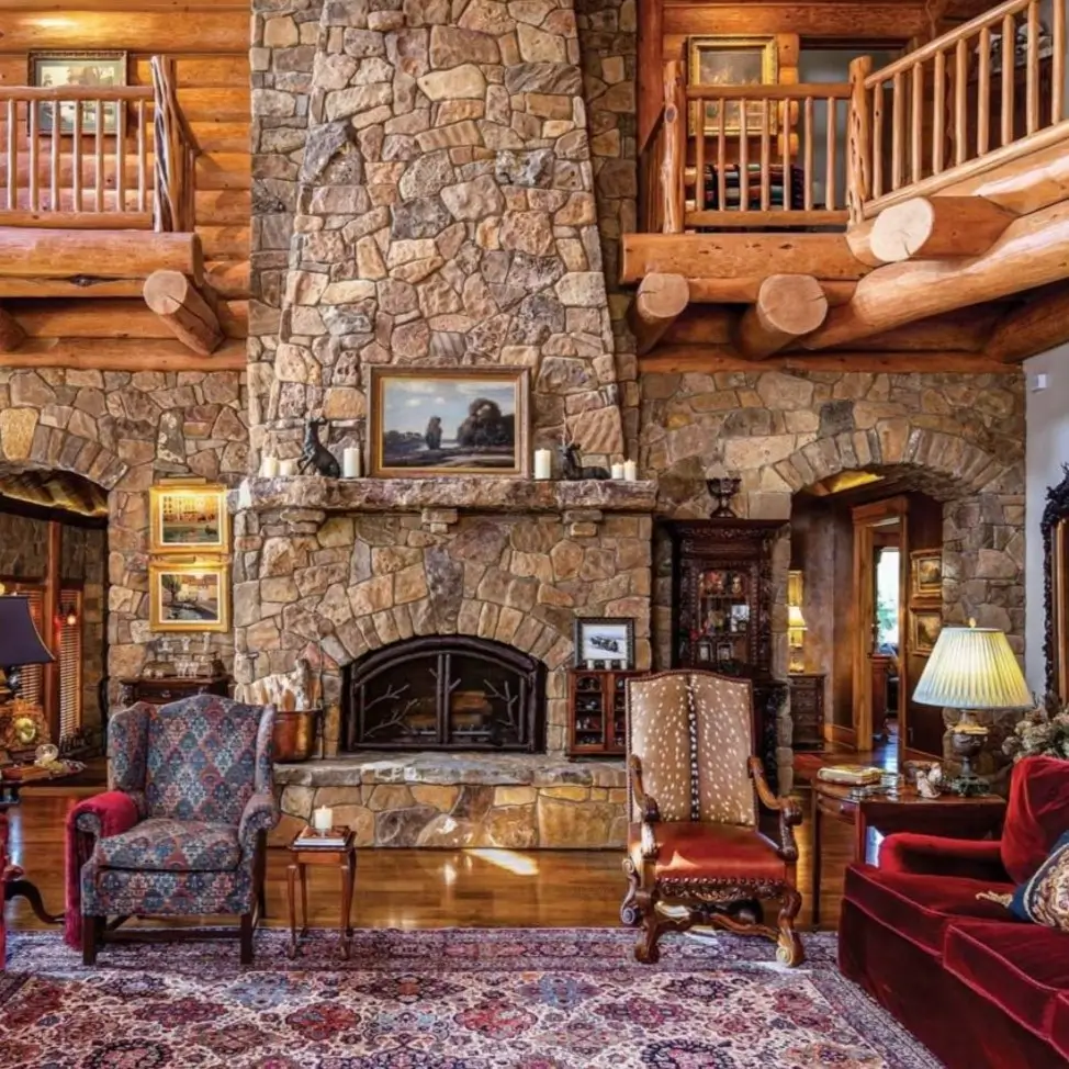 Grand log cabin living room with massive stone fireplace, high ceilings, and exposed logs.