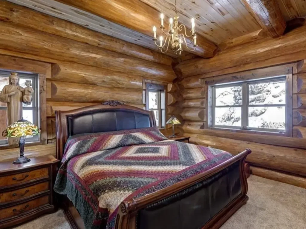 Cozy log cabin bedroom with wooden bed, leather headboard, and patterned quilt.