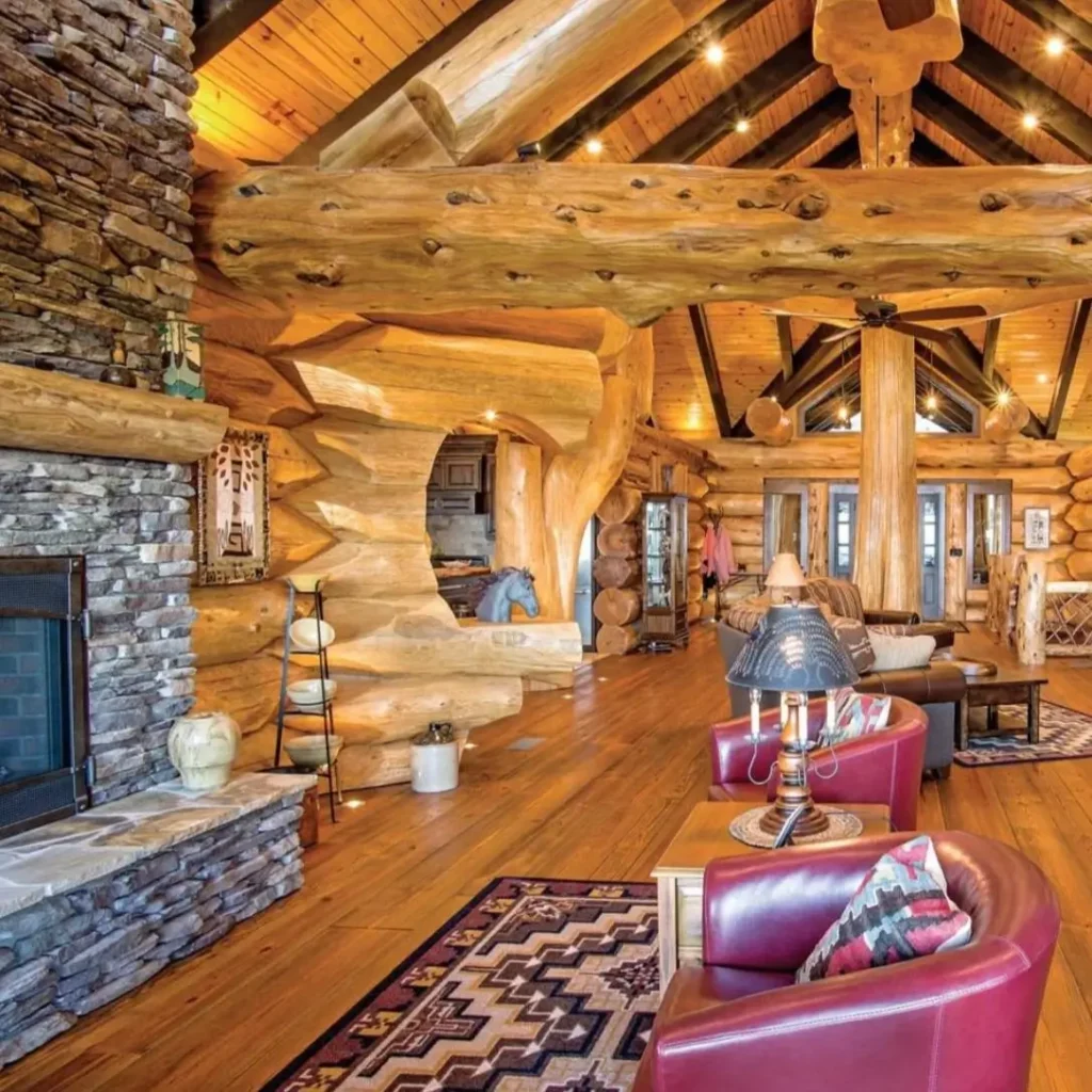 Spacious log cabin living room with red leather armchairs and stone fireplace.