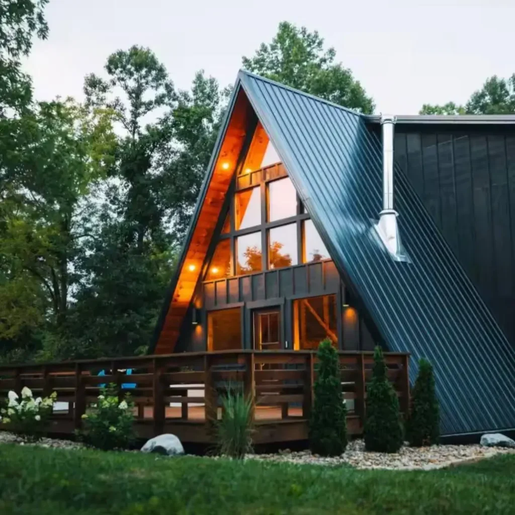 A modern A-frame cabin in the woods featuring a striking contrast between dark siding and warm wood trim.