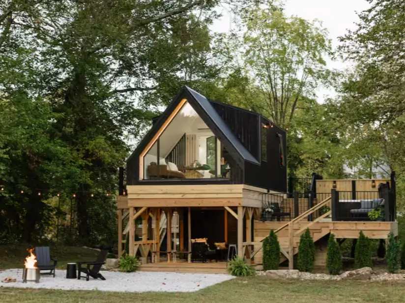 A modern elevated black A-frame cabin in Ohio with a lower patio and outdoor fire pit.