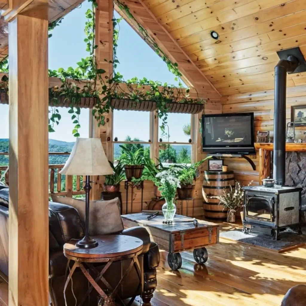 Log cabin living room with large windows, wood stove, and green plants.