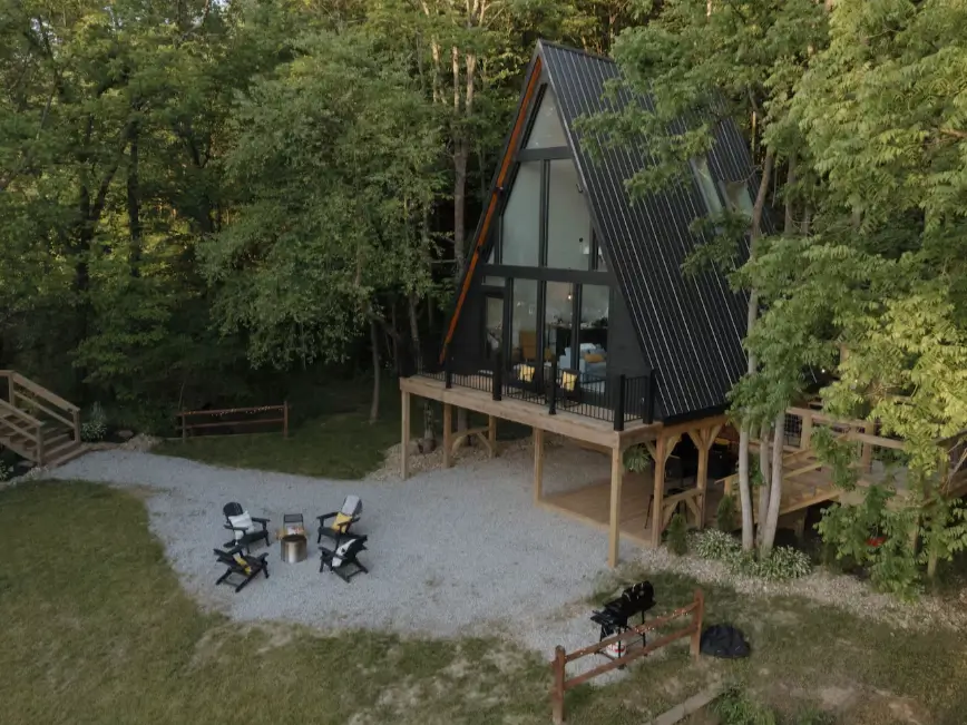 Elevated black A-frame cabin in Hocking Hills with a spacious gravel yard and a modern fire pit area, ideal for families.