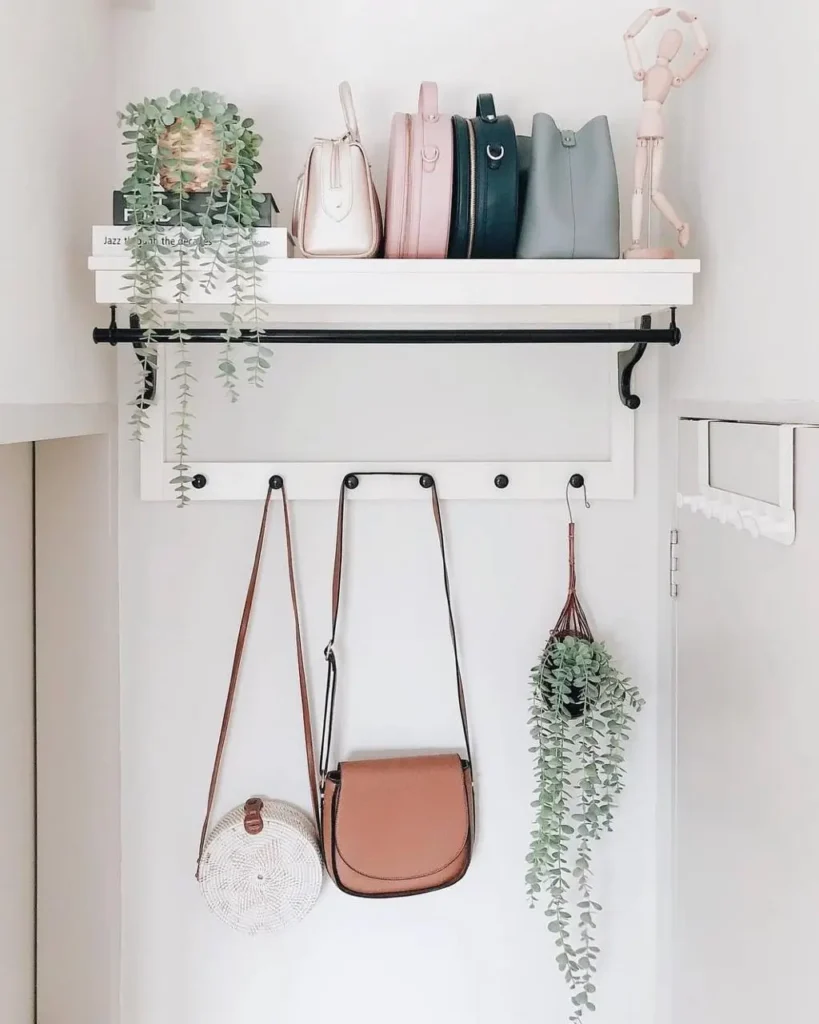 A white entryway shelf with hooks holding bags and displaying plants, a simple small apartment decorating idea.