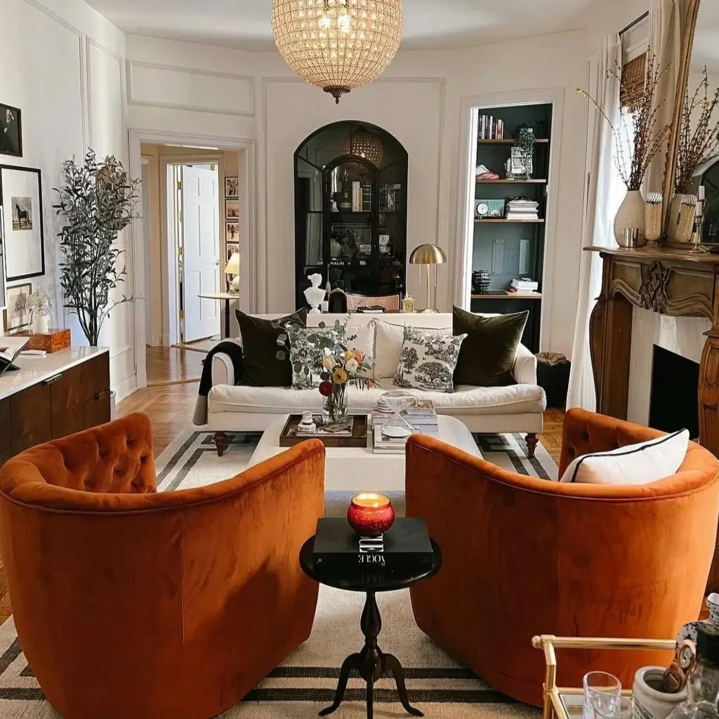 A chic living room with two burnt orange velvet accent chairs, a stylish small apartment design idea on a budget.