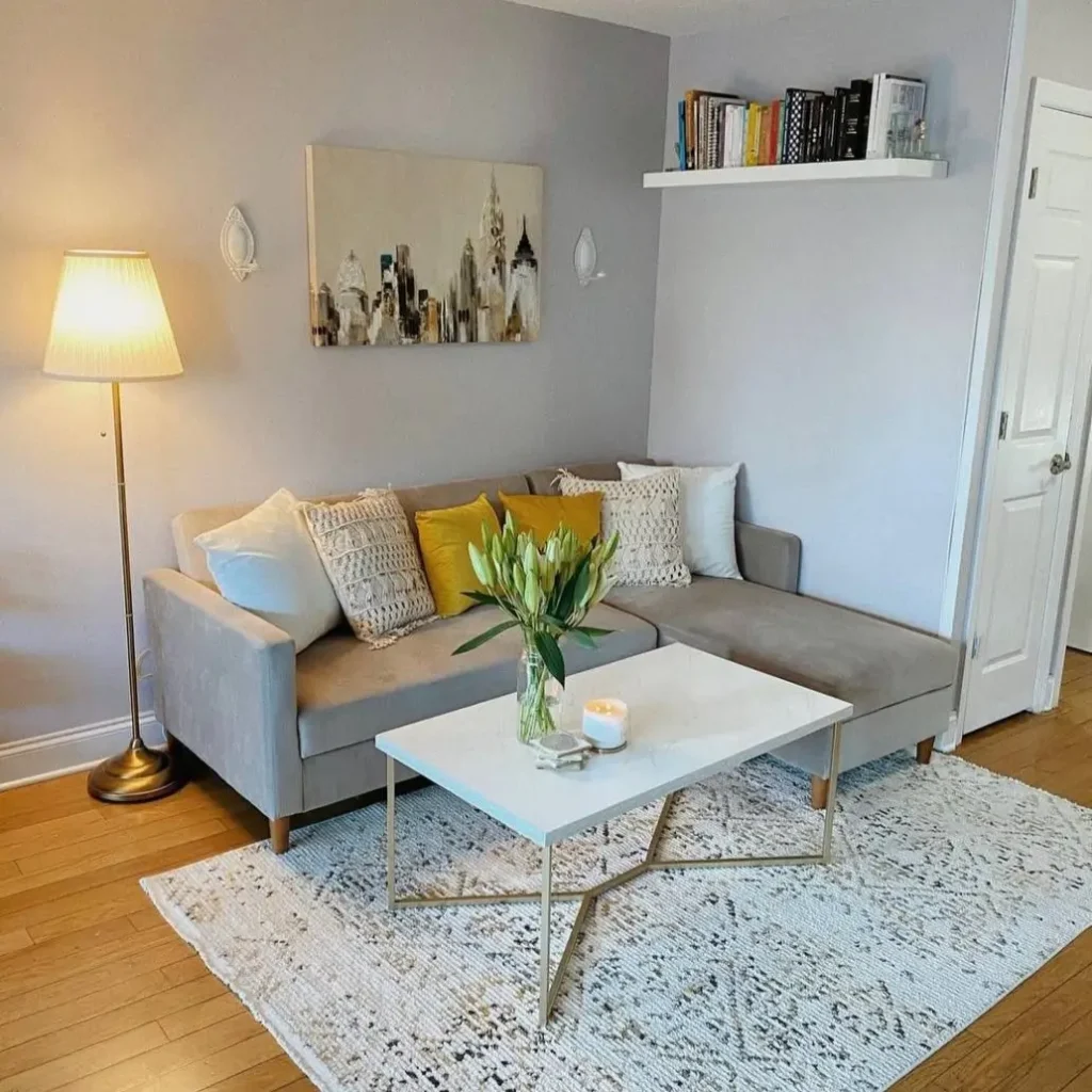 A cozy living room corner with a gray sectional sofa and a white floating shelf for books, a simple small apartment decorating idea.